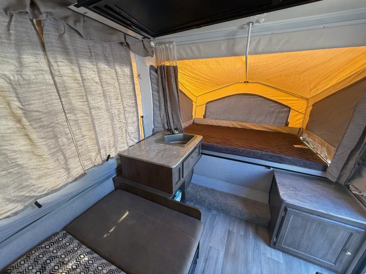 Explore this cozy pop-up camper interior with a bed, kitchen sink, and dinette seating, perfect for an RV rental.. Forest River Flagstaff M.A.C. 2022