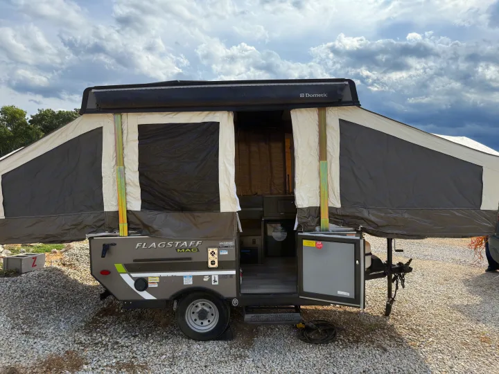 Pop-up camper RV rental, a Flagstaff MAC, set up on gravel under a cloudy sky with its side door open, revealing the interior.. Forest River Flagstaff M.A.C. 2022