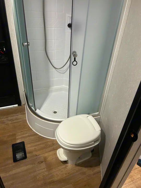 RV rental interior: compact bathroom with a corner shower, white toilet, and wood-look flooring.. Forest River Cherokee 2021