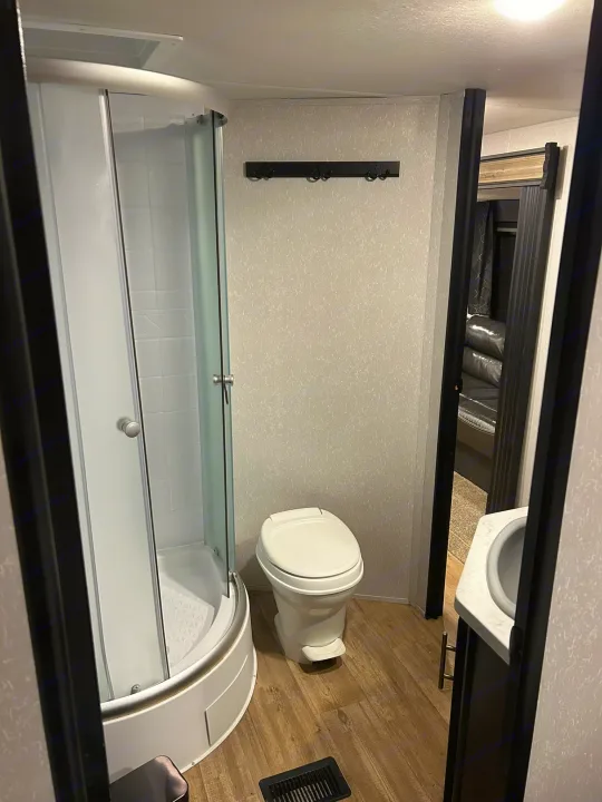 Inside an RV rental bathroom: a compact stand-up shower, toilet, and sink visible through the doorframe.. Forest River Cherokee 2021