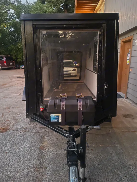 Compact black RV rental camper trailer with a transparent front panel, external battery box, and hitch, parked outdoors.. Custom Squaredrop Trailer 2020