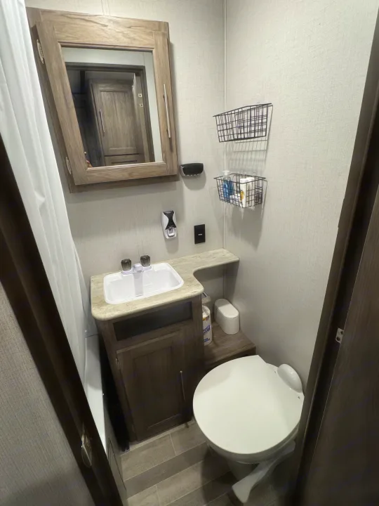 This RV rental bathroom features a sink, toilet, medicine cabinet, and practical wall storage baskets for essentials.. Crossroads RV Zinger 2020