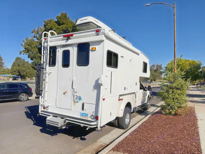 Large white RV rental truck camper, equipped with a ladder & roof rack, parked on a sunny Nevada street.. Ford F350 Diesel Double Cab 2017