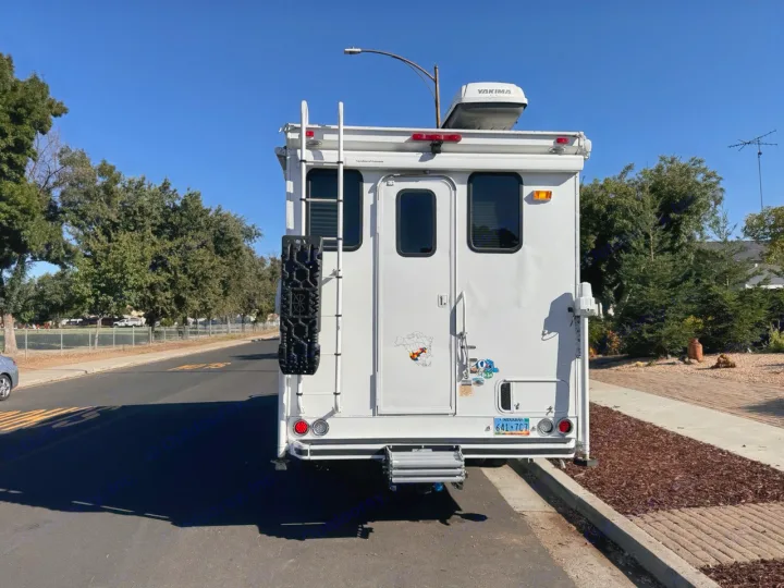 White truck camper, great for an RV rental, parked on a sunny street. Features a ladder, recovery boards, Yakima roof box, Nevada plate.. Ford F350 Diesel Double Cab 2017