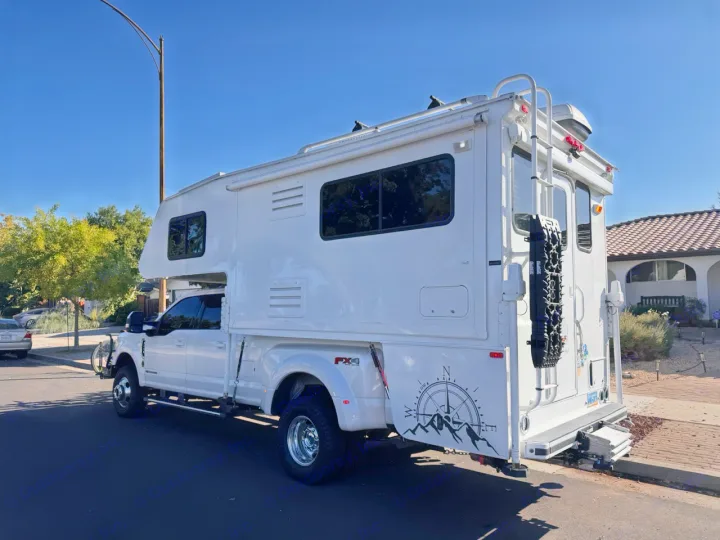 Large white truck camper on a Ford dually with off-road gear, like an RV rental, parked on a sunny residential street.. Ford F350 Diesel Double Cab 2017