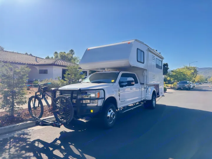 Adventure-ready RV rental: White Ford truck camper with a mountain bike, parked on a sunny suburban street.. Ford F350 Diesel Double Cab 2017