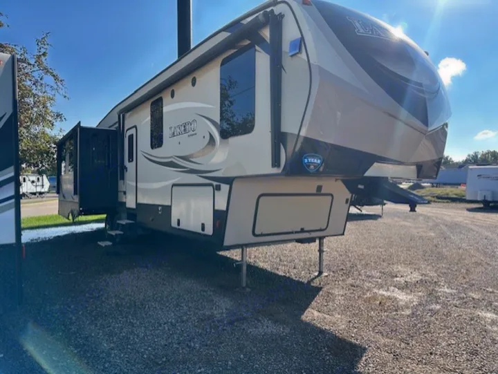 This spacious beige and black fifth-wheel RV, ideal for an rv rental, features an extended slide-out on a sunny gravel lot.. Keystone RV Laredo 2018