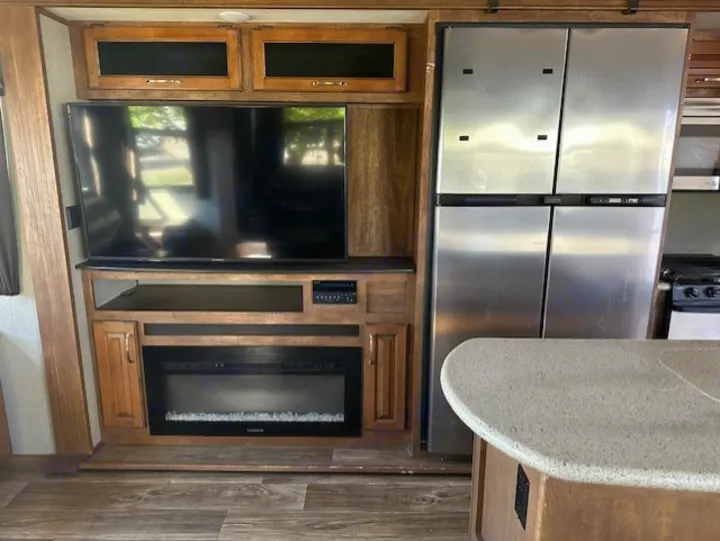 RV rental living area: Features a large TV, electric fireplace, and stainless steel refrigerator. Kitchen island visible.. Keystone RV Laredo 2018