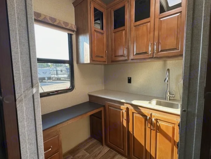 Explore this rv rental's functional interior: kitchen sink, wooden cabinets, a bright window, and a convenient built-in desk.. Keystone RV Laredo 2018
