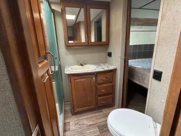 Inside an RV rental: a compact bathroom with vanity, sink, mirrored cabinet, toilet, shower, and a peek into the bedroom.. Keystone RV Laredo 2018