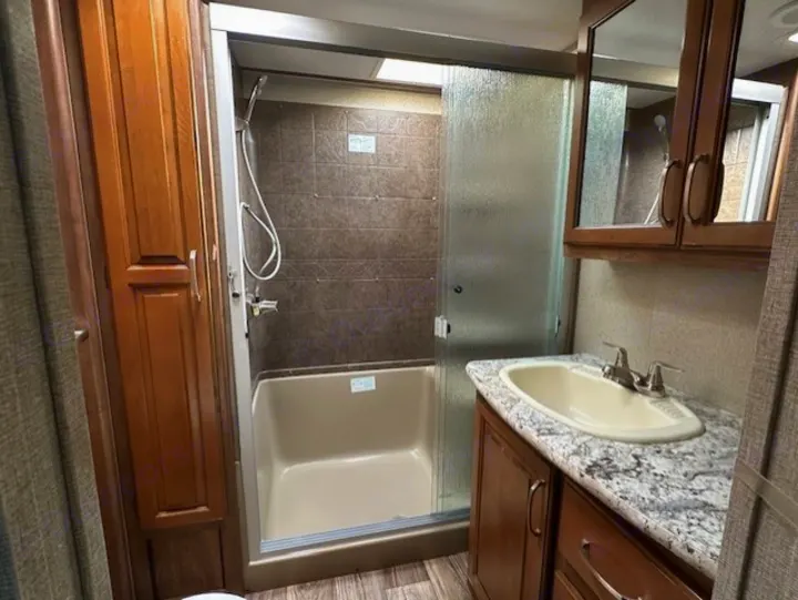 Clean RV rental bathroom featuring a shower-tub combo, vanity with sink, and ample wood cabinetry.. Keystone RV Laredo 2018