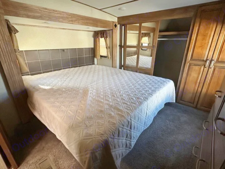 Spacious rv rental bedroom featuring a comfy bed, padded headboard, mirrored closet, and dresser for ample storage.. Keystone RV Laredo 2018