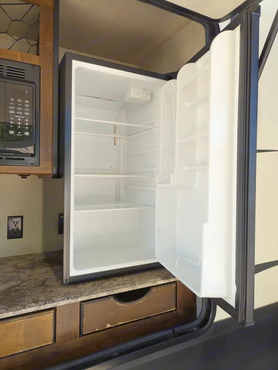 Compact rv rental kitchen with an open, empty mini-fridge and microwave, ready for your next adventure.. Grand Design Reflection 2019