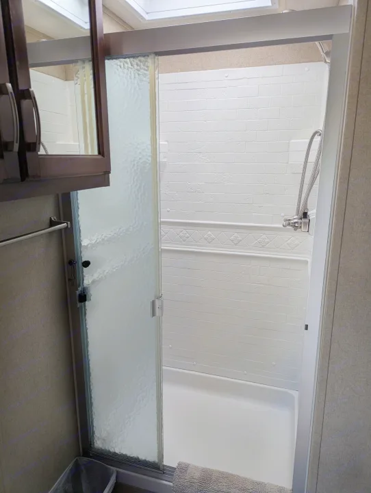 Compact white shower with sliding frosted glass door, textured walls, and a flexible showerhead in an rv rental bathroom.. Grand Design Reflection 2019