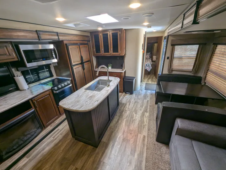 Spacious RV rental showcasing a full kitchen with island sink, stove, fridge, and a cozy living/dining area.. Grand Design Reflection 2019