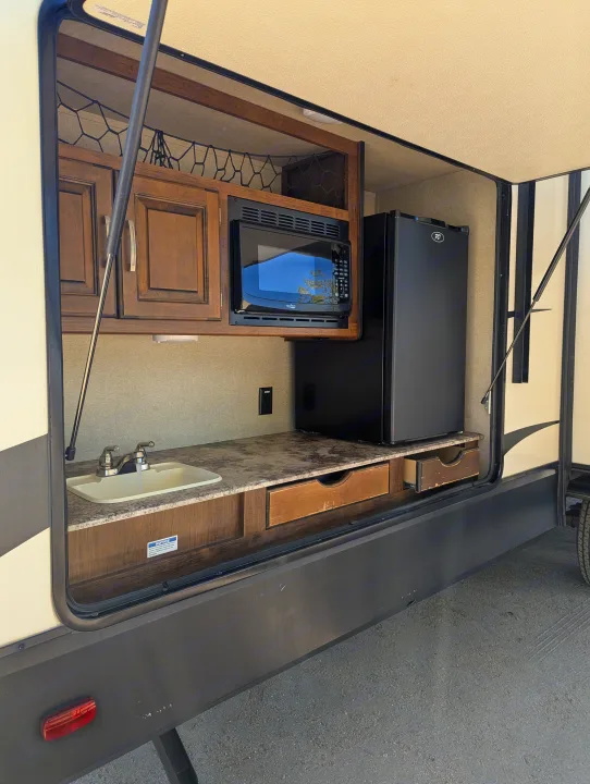 This RV rental's outdoor kitchen features a microwave, mini-fridge, sink, and storage for easy open-air cooking.. Grand Design Reflection 2019
