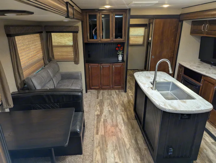 Spacious rv rental interior featuring a kitchen island with sink, dining booth, sofa, and warm wood-look flooring.. Grand Design Reflection 2019