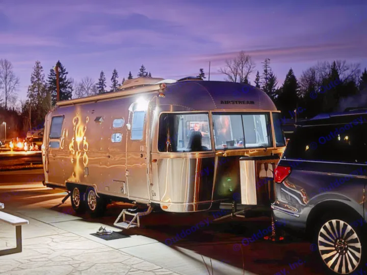 An illuminated Airstream rv rental parked at dusk, person visible inside, alongside an SUV under a purple sky.. Airstream International 2018