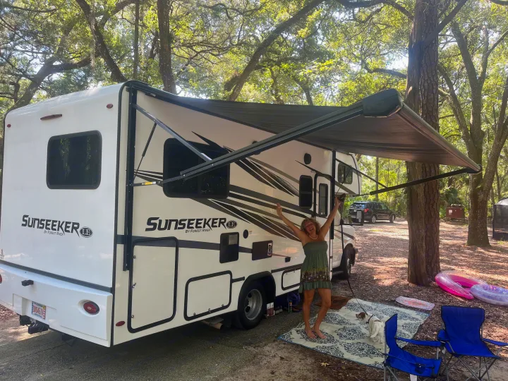 Excited woman and dog enjoying their rv rental at a sunny campground with an extended awning.. Forest River Sunseeker LE 2023