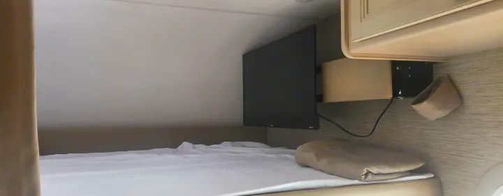 Cozy RV rental bunk bed area with a mounted TV, crisp white sheets, and practical wall storage for comfortable travel.. Thor freedom elite 2022