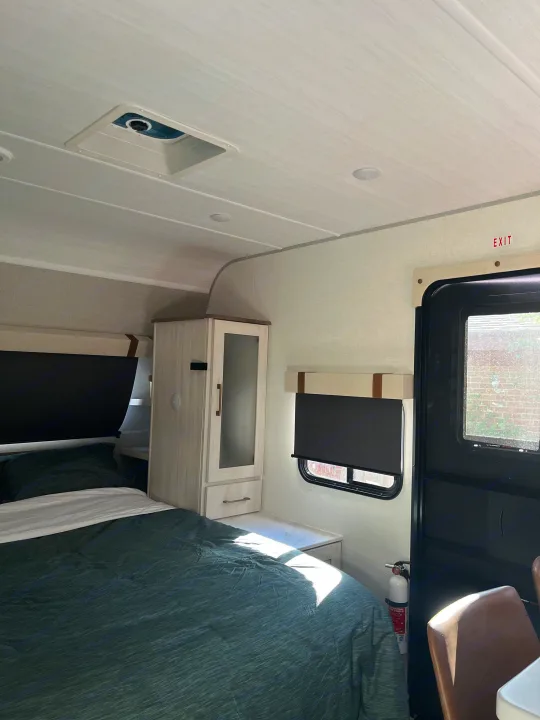 RV rental interior: A bright, modern bedroom area with a green bed, storage, window, & safety exit.. Forest River 5NHTRDV27TD211453 2026
