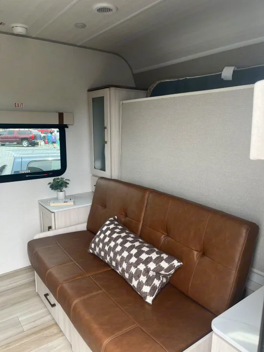 Cozy rv rental interior with a brown sofa bed, checkered pillow, sleek cabinets, and a window offering an outdoor view.. Forest River 5NHTRDV27TD211453 2026