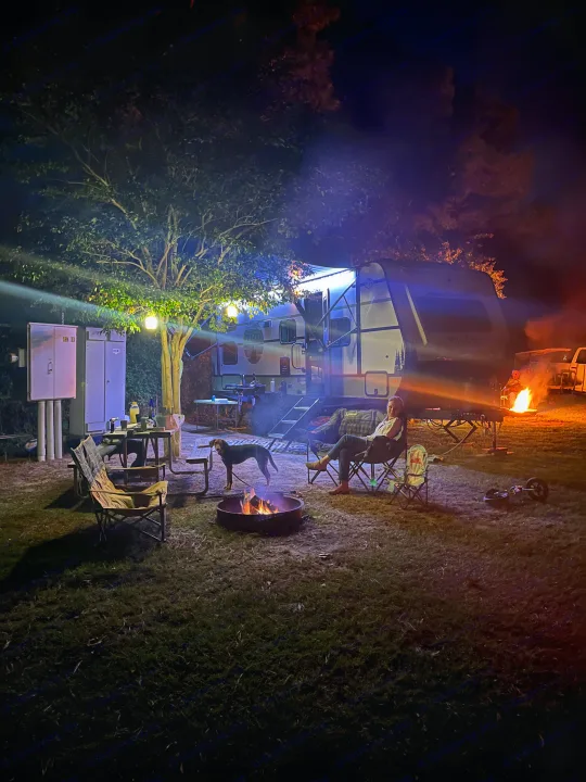 Cozy evening at an RV rental campsite: a person, a dog, and a campfire illuminate the night by a travel trailer.. Forest River 5NHTRDV27TD211453 2026