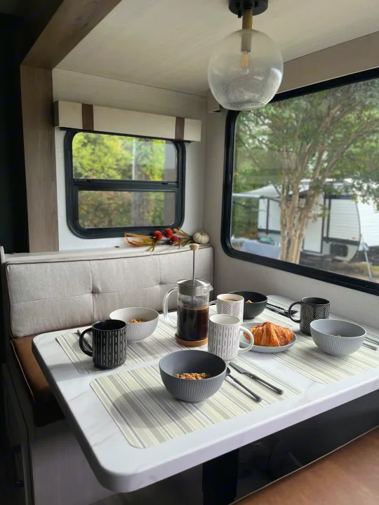A pleasant RV rental dining area, set for breakfast with coffee, croissants, and cereal, overlooking the campsite.. Forest River 5NHTRDV27TD211453 2026