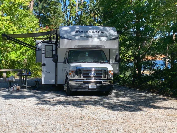 A Sunseeker RV rental by Forest River at a scenic campsite with a picnic table, trees, and lake view.. Forest River Sunseeker LE 2022