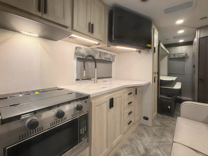 Inside this RV rental, a compact kitchen features a stove, sink, cabinets, and a TV, optimizing space for travelers.. Forest River Sunseeker LE 2022
