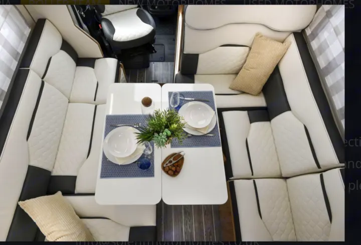 RV rental motorhome interior: A cozy dining area with white & black quilted L-shaped seating and two tables set for two, perfect for camper travel.. Roller Team 707 Auto Roller 2025
