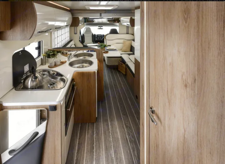 Interior of a modern rv rental, showcasing a functional kitchen, cozy dining space, light wood cabinetry, and dark plank flooring.. Roller Team 707 Auto Roller 2025