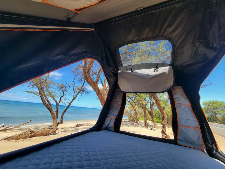 Inside a comfy rooftop tent from your RV rental, enjoy stunning beach and ocean views, framed by tropical trees.. Jeep Gladiator 2022