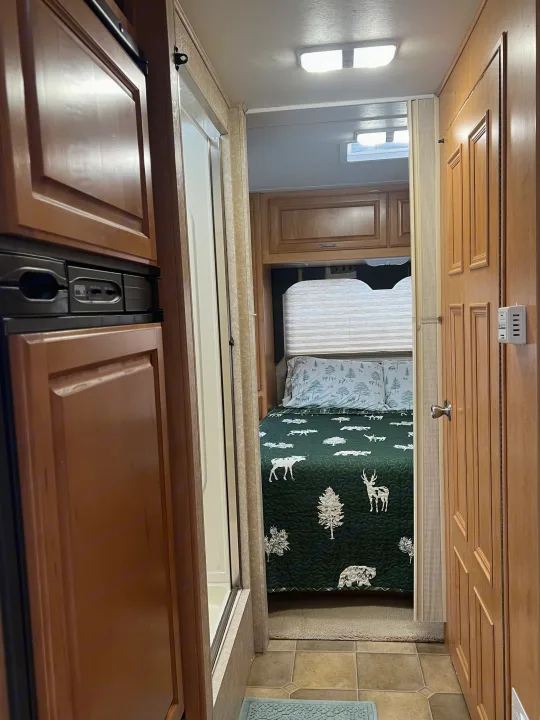 Cozy RV rental interior, showing a bedroom with a nature-themed quilt, cabinetry, refrigerator, and a shower stall in a narrow hallway.. Four Winds 5000 2006