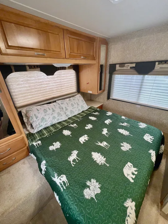 Cozy RV rental bedroom with a forest-themed comforter, pillows, wood cabinets, and window blinds, ready for a comfortable stay.. Four Winds 5000 2006