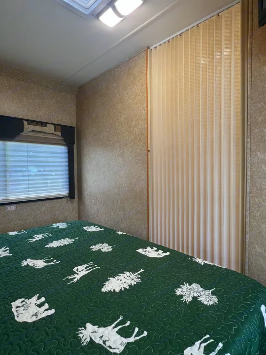 RV rental bedroom with patterned green quilt, window, and pleated privacy door.. Four Winds 5000 2006