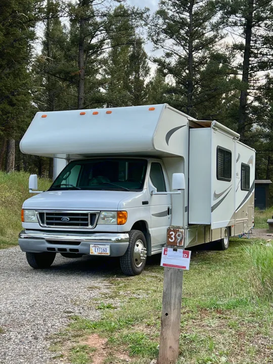 White rv rental parked at campsite 39 with a slide-out, surrounded by tall pines. Perfect for outdoor adventures.. Four Winds 5000 2006