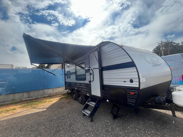 A sleek grey and black travel trailer, ready for your next rv rental adventure, with its awning open under a cloudy sky.. Forest River Cherokee 2019