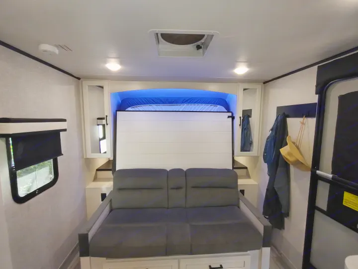 Modern RV rental interior showcasing a convertible sofa and murphy bed with blue lighting, a window, and storage.. Jayco Jay Feather Air 18mbh 2024