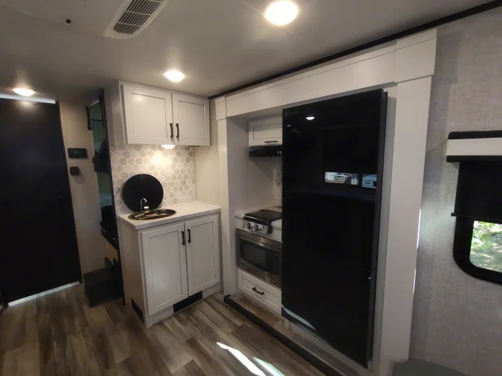 Bright RV rental kitchen with light cabinets, hexagonal backsplash, sink, stove, microwave, and sleek black fridge.. Jayco Jay Feather Air 18mbh 2024
