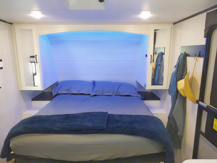 Cozy RV rental bedroom featuring a bed with blue ambient lighting and integrated storage on either side.. Jayco Jay Feather Air 18mbh 2024