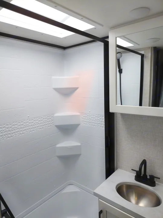 Step into this bright, modern RV rental bathroom featuring a spacious shower with skylight, shelves, and a sleek vanity with sink.. Jayco Jay Feather Air 18mbh 2024