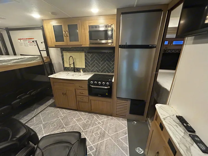 Modern RV rental interior featuring a full kitchen with a fridge, stove, and microwave, plus bunk beds and recliners.. Work and Play Toy Hauler 2022