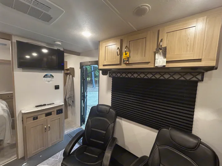 RV rental's inviting interior: features a TV, wood cabinets, dark blinds, and two comfortable recliners. Door open to outside view.. Work and Play Toy Hauler 2022