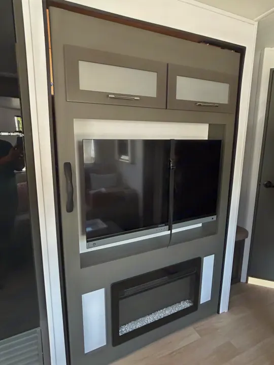 Stylish RV rental entertainment unit: gray cabinets, TV, & electric fireplace, perfect for compact living.. Keystone RV Bullet Crossfire 2025