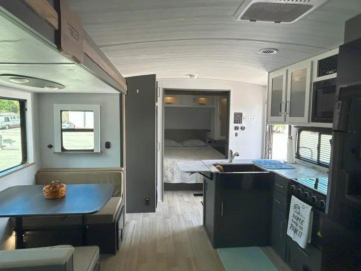 Step inside this bright rv rental, revealing a kitchen, dining booth, and private bedroom with light wood floors and modern grey accents.. Keystone RV Bullet Crossfire 2025