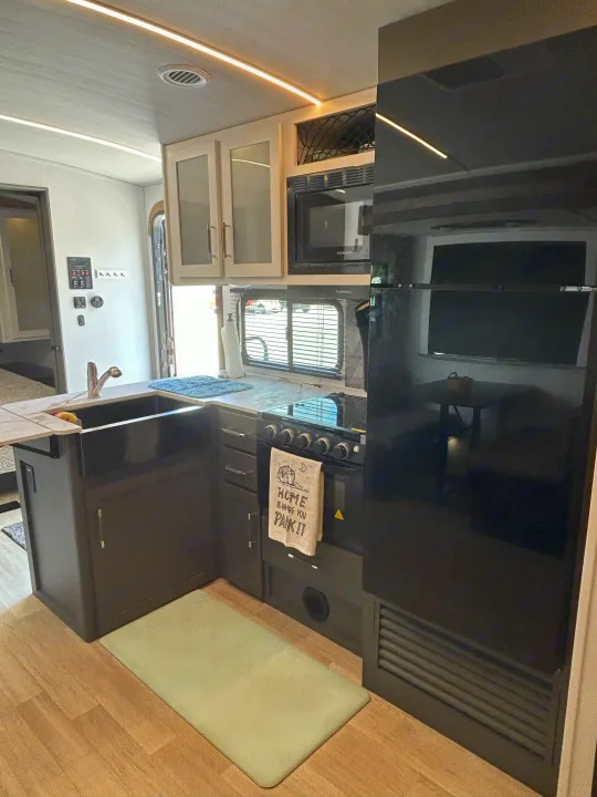 Modern RV rental kitchen with dark cabinets, stainless steel appliances, and ceiling lights, ready for adventure.. Keystone RV Bullet Crossfire 2025