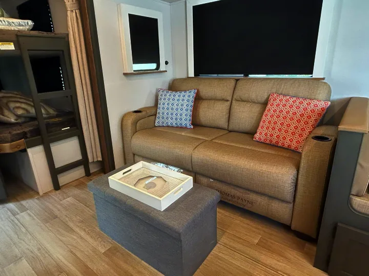 Cozy RV rental interior featuring a comfy sofa with patterned pillows, bunk beds, and a versatile storage ottoman.. Keystone RV Bullet Crossfire 2025
