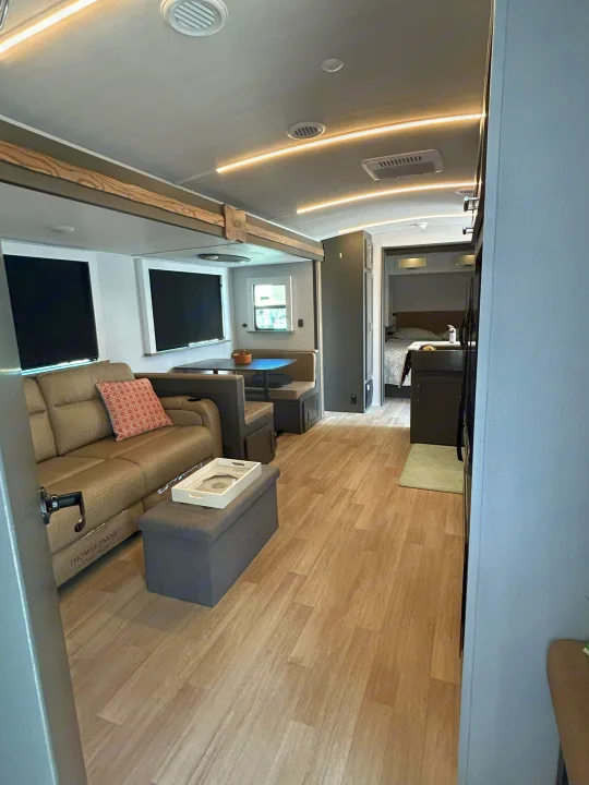 Inside this modern RV rental: a light-filled living area with sofa, dining booth, and peek into the bedroom.. Keystone RV Bullet Crossfire 2025