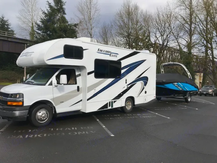 Freedom Elite RV rental towing a blue jet ski on a trailer, parked on asphalt. Ready for water recreation.. Thor Freedom Elite 2021